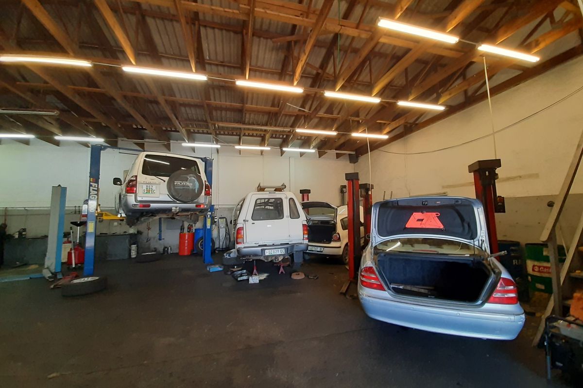 A functional automotive workshop garage featuring multiple vehicle lifts, exposed timber roof trusses, and industrial fluorescent lighting.