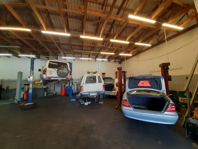 A functional automotive workshop garage featuring multiple vehicle lifts, exposed timber roof trusses, and industrial fluorescent lighting.