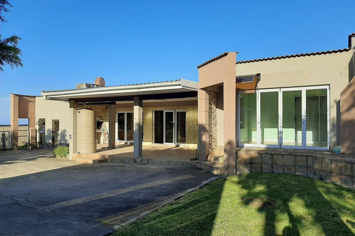 Rear view of the farm property featuring a spacious covered patio with a built-in braai, water tank, and large sliding glass doors.