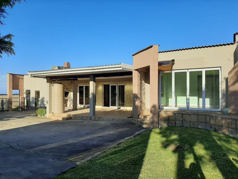 Rear view of the farm property featuring a spacious covered patio with a built-in braai, water tank, and large sliding glass doors.