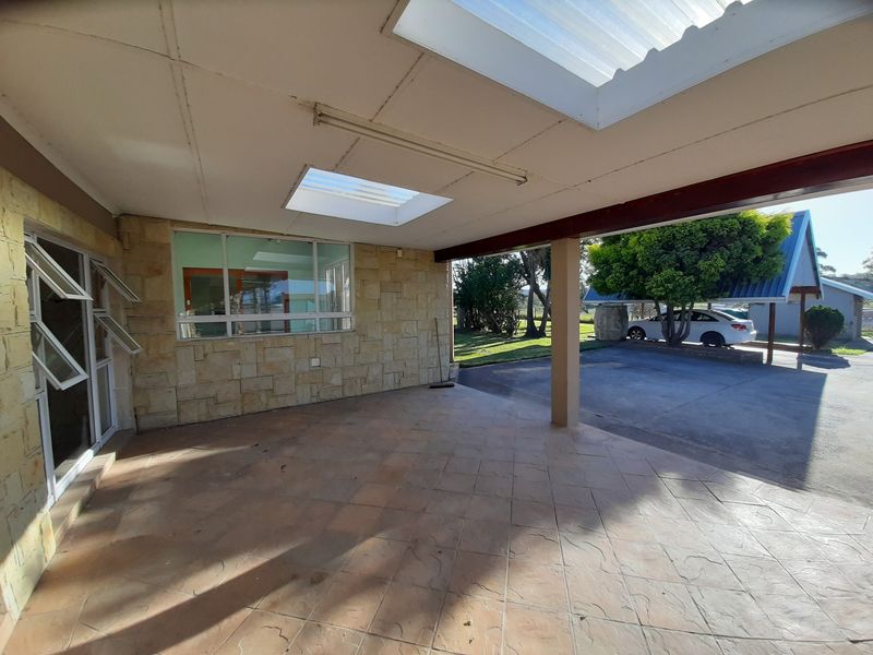 A covered patio area featuring stone cladding, skylights, and tiled flooring, providing a functional outdoor space overlooking the driveway and garden.