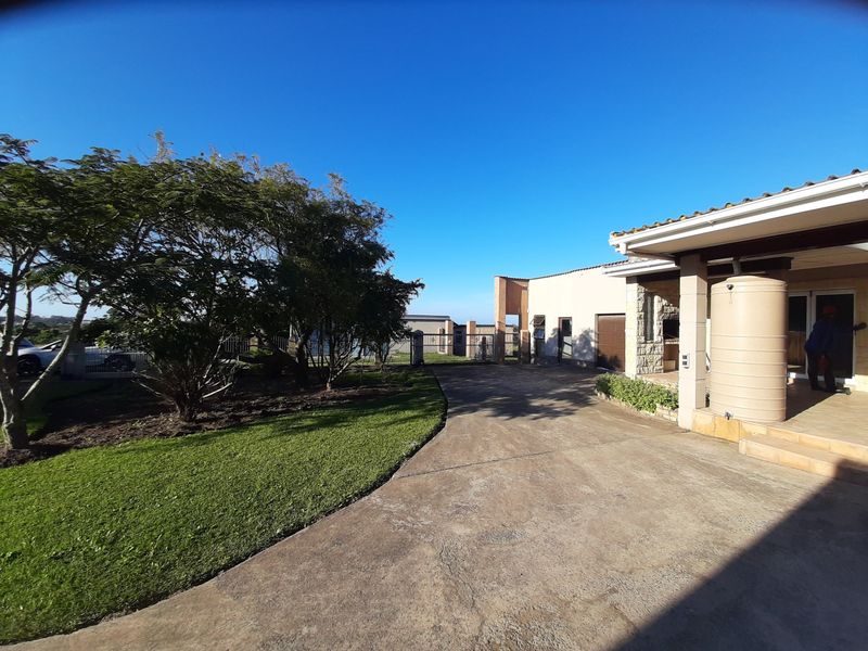Front exterior view of the farm property featuring a concrete driveway, water storage tank, and a covered patio area with stone cladding details.
