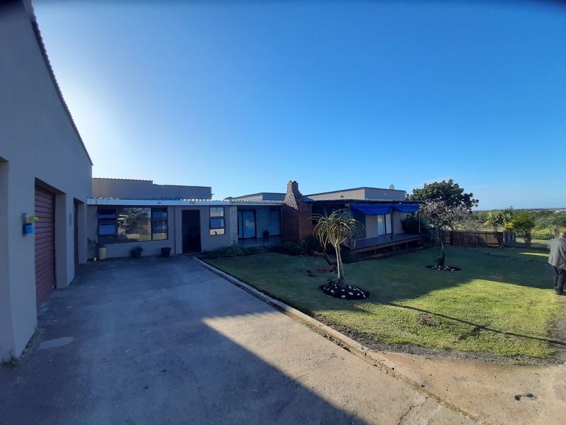 Rear view of the farm property featuring a concrete driveway, lawn area, and a covered patio with a brick chimney.