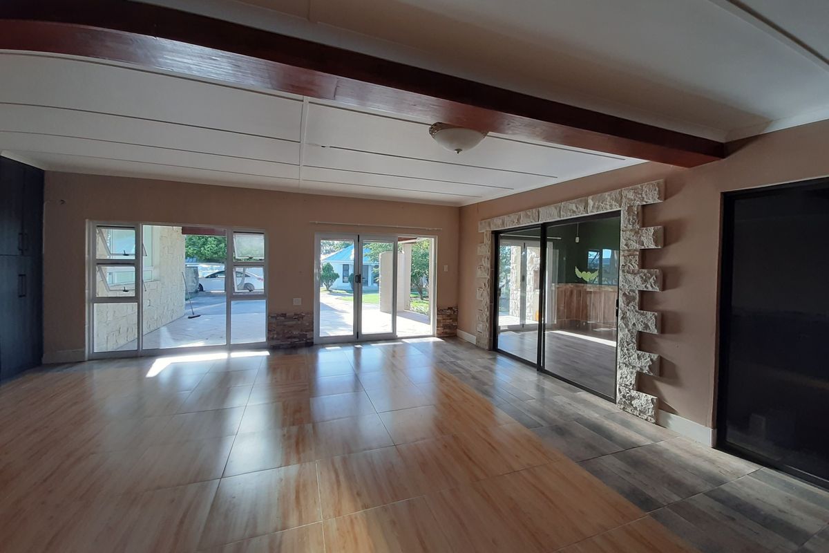 Spacious, light-filled living area featuring tiled floors, exposed timber ceiling beams, and stone-clad accents with multiple sliding glass doors leading to the exterior.