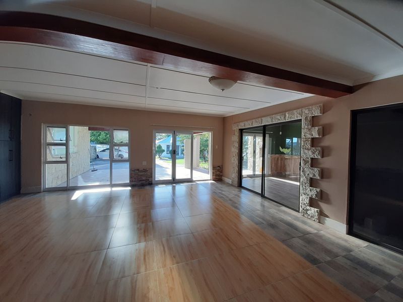Spacious, light-filled living area featuring tiled floors, exposed timber ceiling beams, and stone-clad accents with multiple sliding glass doors leading to the exterior.