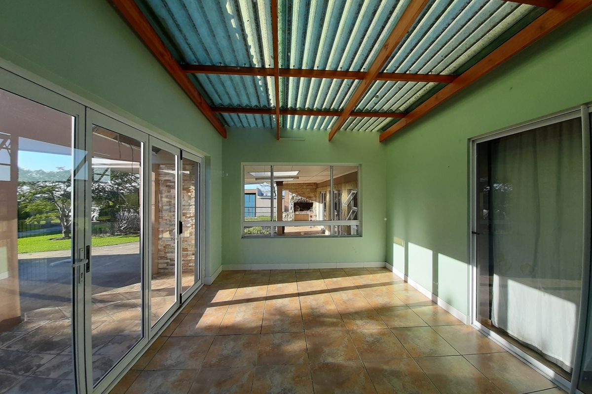A bright, enclosed patio area featuring tiled flooring, exposed timber rafters, and large aluminium sliding doors providing seamless access to the garden.