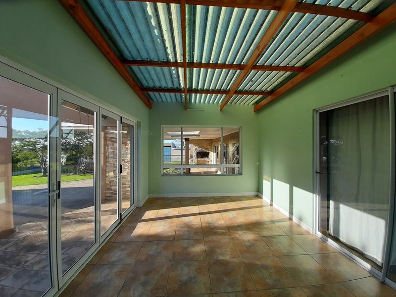 A bright, enclosed patio area featuring tiled flooring, exposed timber rafters, and large aluminium sliding doors providing seamless access to the garden.