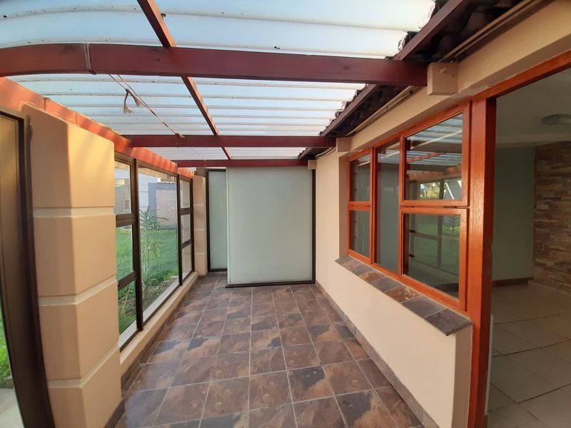 A covered patio area featuring tiled flooring, timber-framed windows, and a translucent roof, providing a bright and sheltered outdoor transition space.