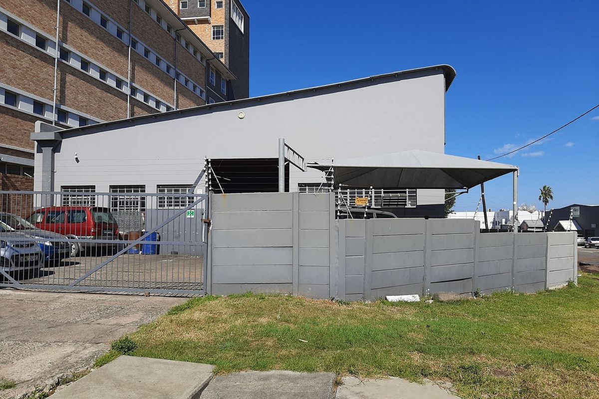 Rear exterior view of the commercial property featuring a secure gated entrance, concrete boundary wall with electric fencing, and a shaded parking area.