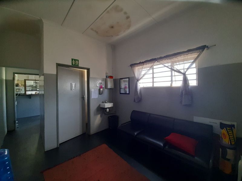 A waiting area or lounge space featuring a wall-mounted basin, security window bars, and visible water damage on the ceiling tiles.