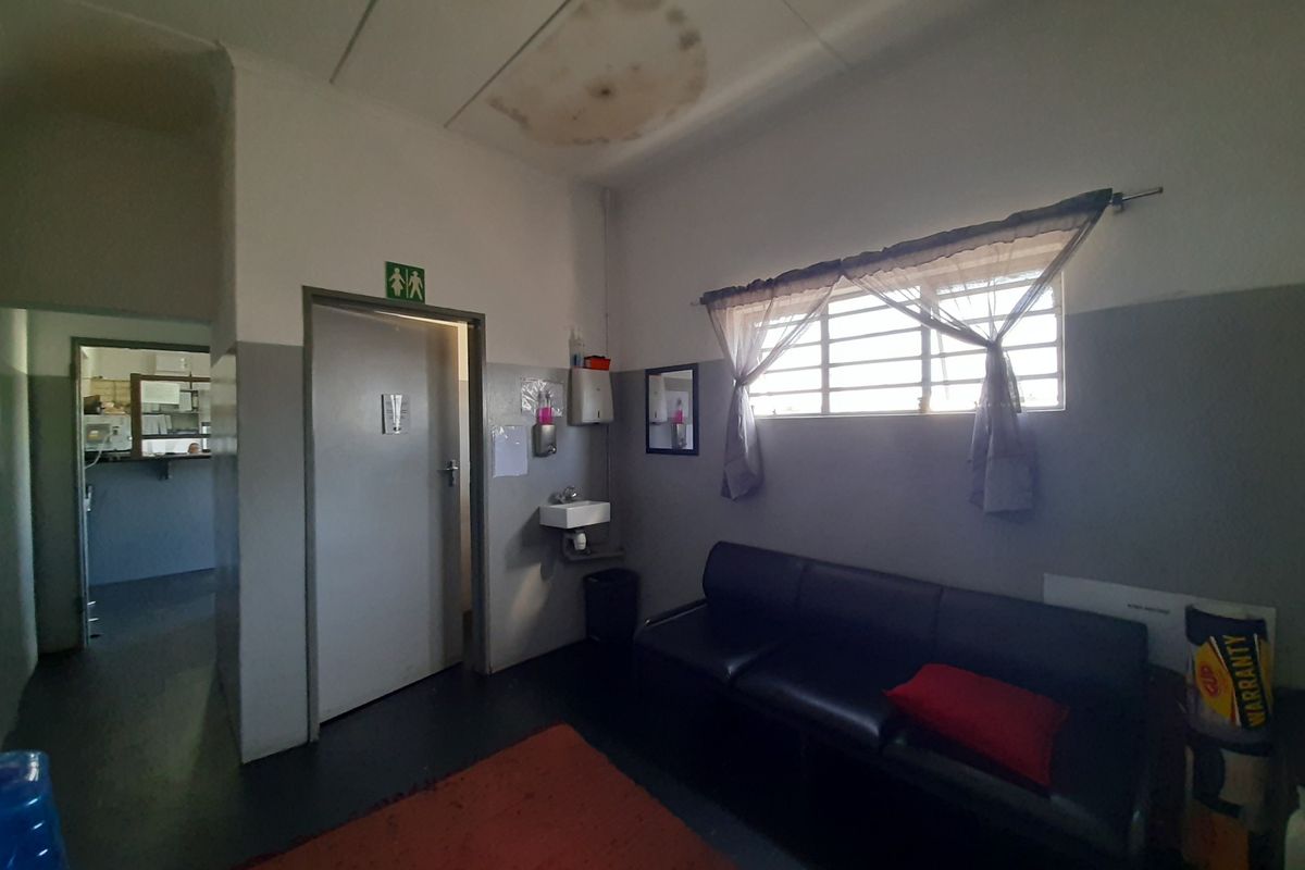 A waiting area or lounge space featuring a wall-mounted basin, security window bars, and visible water damage on the ceiling tiles.