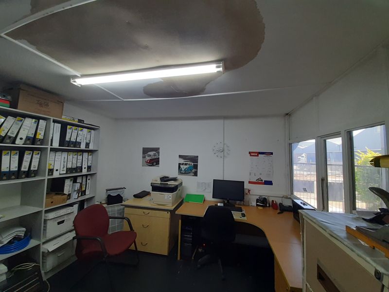A functional office space featuring built-in shelving and large windows, currently showing significant water damage on the ceiling requiring immediate attention.