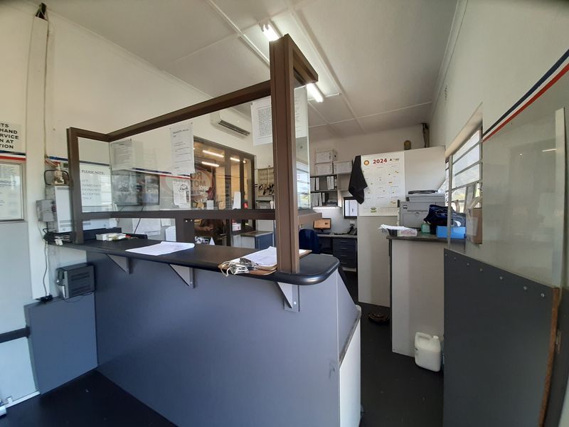 Commercial office space featuring a built-in reception counter with a glass security partition, split-system air conditioning, and functional louvered windows.