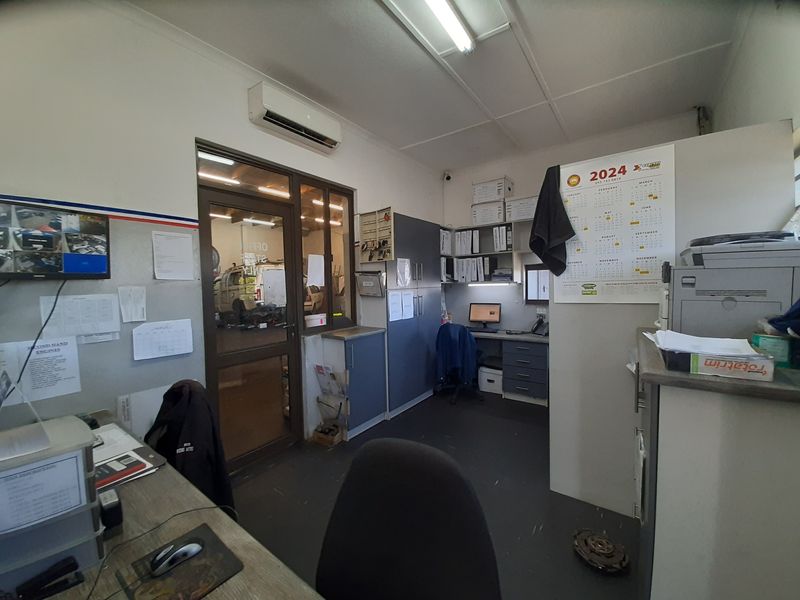 A functional commercial office space featuring built-in cabinetry, a split-system air conditioner, and a glass-paneled door providing visibility into the workshop area.