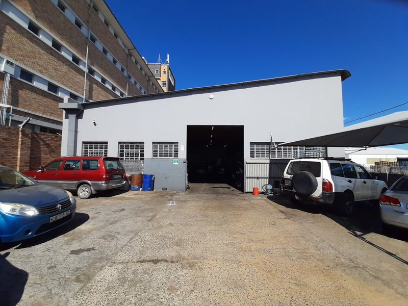 Commercial industrial unit featuring a large roller shutter door, concrete driveway, and attached shade cloth carport for vehicle access.