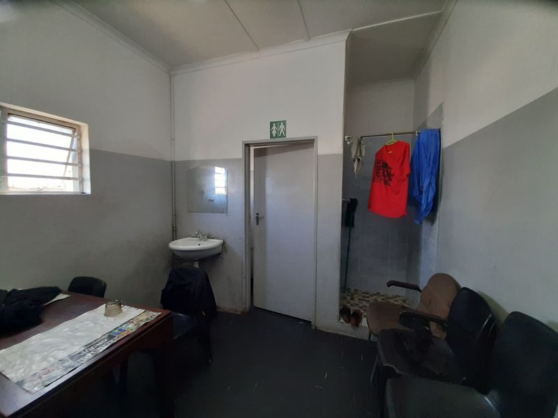 A functional commercial bathroom area featuring a wall-mounted basin, shower cubicle, and security-barred window, requiring cosmetic refurbishment and deep cleaning.