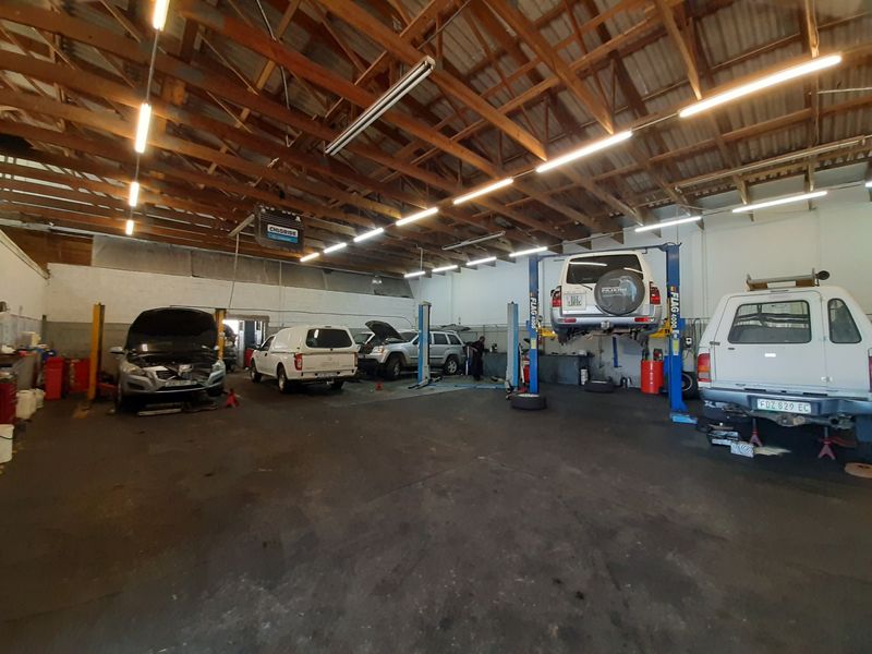 Spacious commercial workshop featuring exposed timber roof trusses, multiple vehicle hydraulic lifts, and durable concrete flooring, suitable for automotive repair operations.