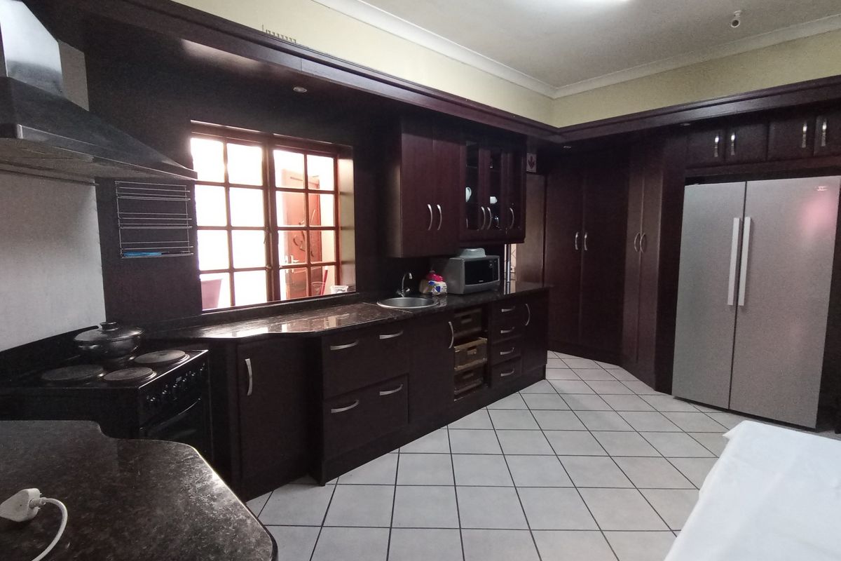 Spacious kitchen featuring dark wood cabinetry, granite countertops, tiled flooring, and integrated appliance space, offering a functional layout for meal preparation.