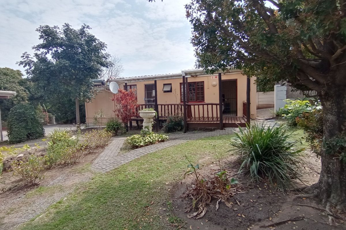 A view of the guest house exterior featuring a wooden deck, paved garden pathways, and established landscaping.