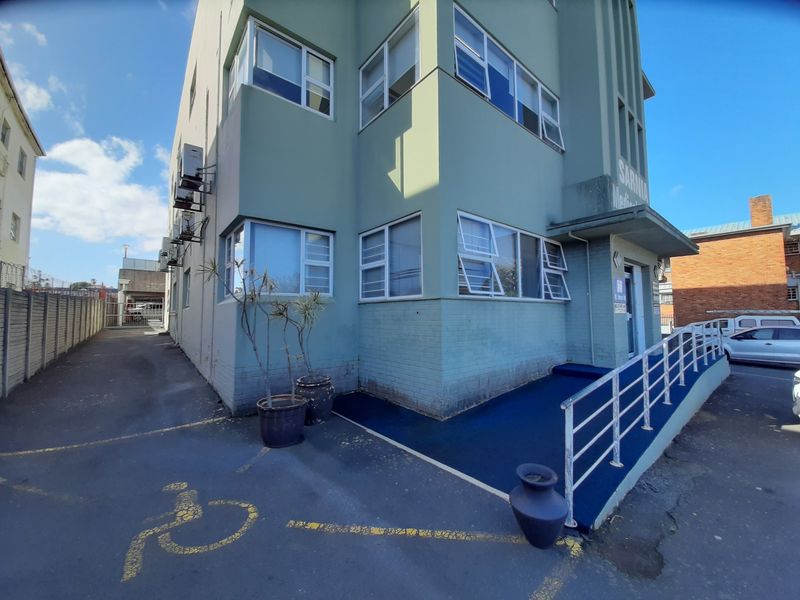 Exterior view of a commercial building featuring a wheelchair-accessible ramp, metal handrails, and external air conditioning units.