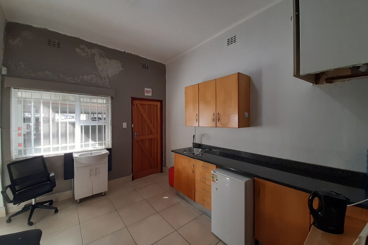 A small kitchenette area featuring built-in wooden cabinetry, a sink, and tiled flooring, currently showing signs of wall surface wear and maintenance needs.
