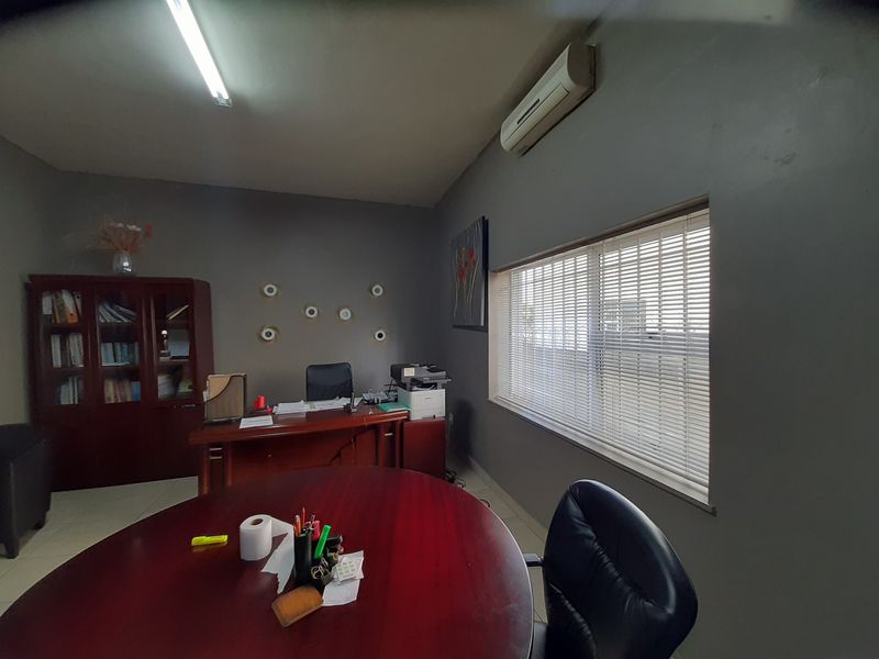 A functional commercial office space featuring tiled flooring, a wall-mounted air conditioning unit, and large windows with venetian blinds for natural light control.