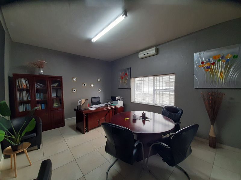 A functional office space featuring tiled flooring, a wall-mounted air conditioning unit, and integrated window blinds, providing a professional environment for business operations.