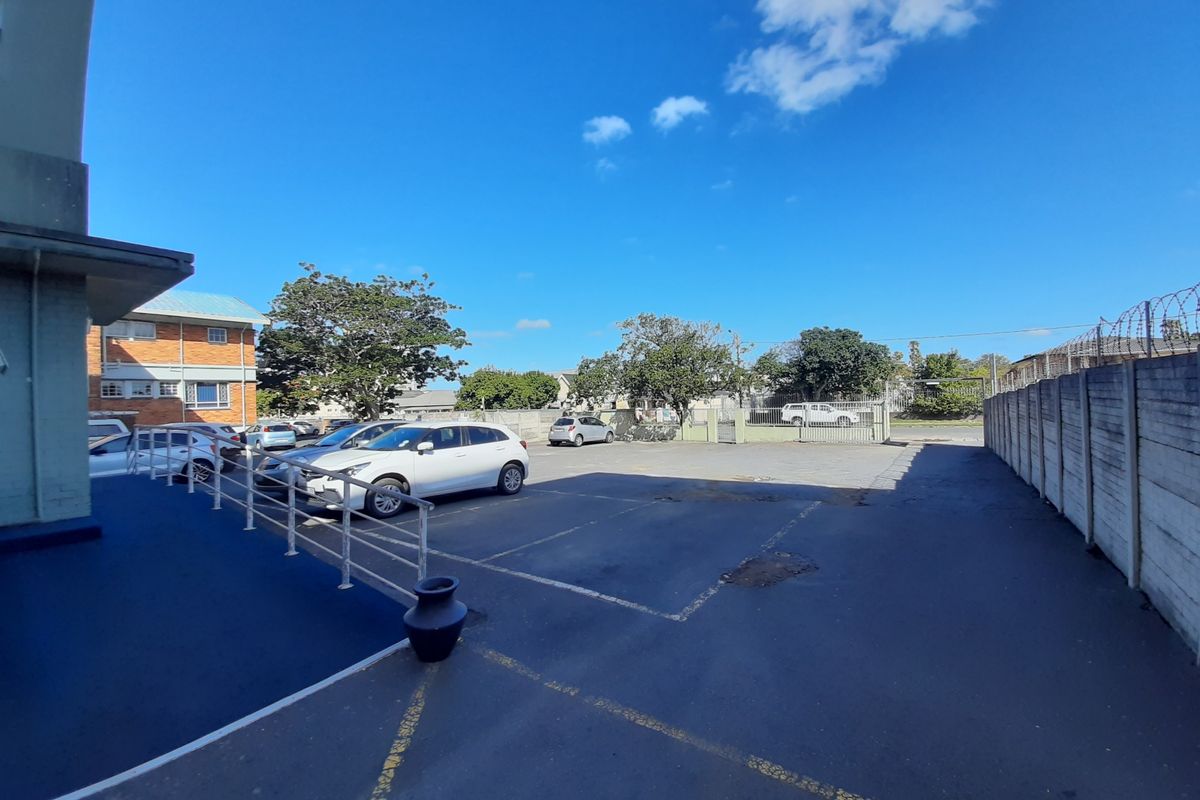 Rear exterior view of the commercial property featuring an asphalt parking area, concrete boundary wall with security fencing, and a painted access ramp.