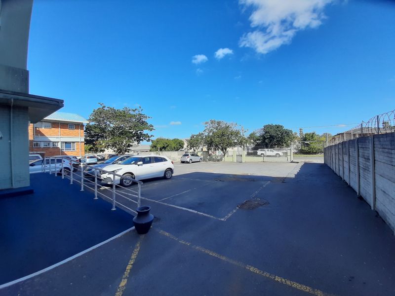 Rear exterior view of the commercial property featuring an asphalt parking area, concrete boundary wall with security fencing, and a painted access ramp.