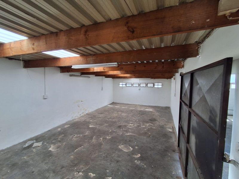 An empty industrial-style garage space featuring exposed timber beams, corrugated metal ceiling, concrete flooring, and natural light from skylights.