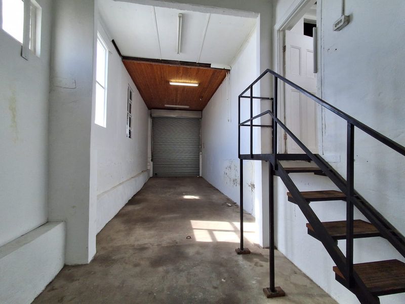 Spacious industrial garage area featuring a roller shutter door, concrete flooring, and an internal metal staircase leading to an upper level.