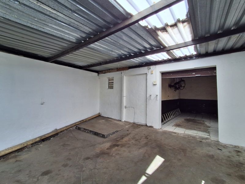 An industrial utility space featuring concrete flooring, steel structural beams, and a partially damaged corrugated metal roof with translucent panels.