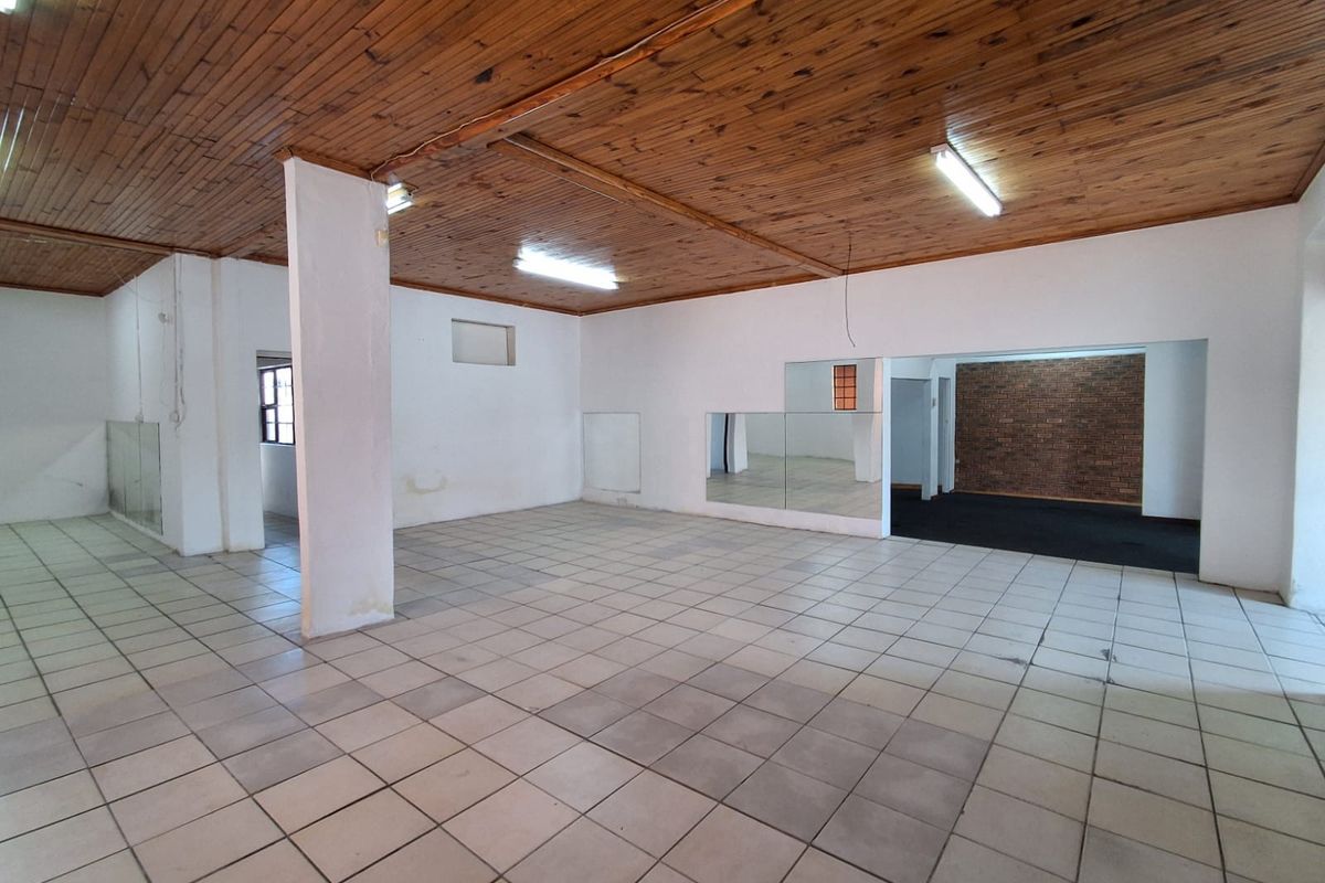 Spacious open-plan industrial area featuring a timber ceiling, ceramic tiled flooring, and an exposed brick accent wall, suitable for various commercial or studio uses.