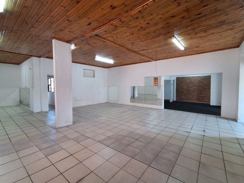 Spacious open-plan industrial area featuring a timber ceiling, ceramic tiled flooring, and an exposed brick accent wall, suitable for various commercial or studio uses.