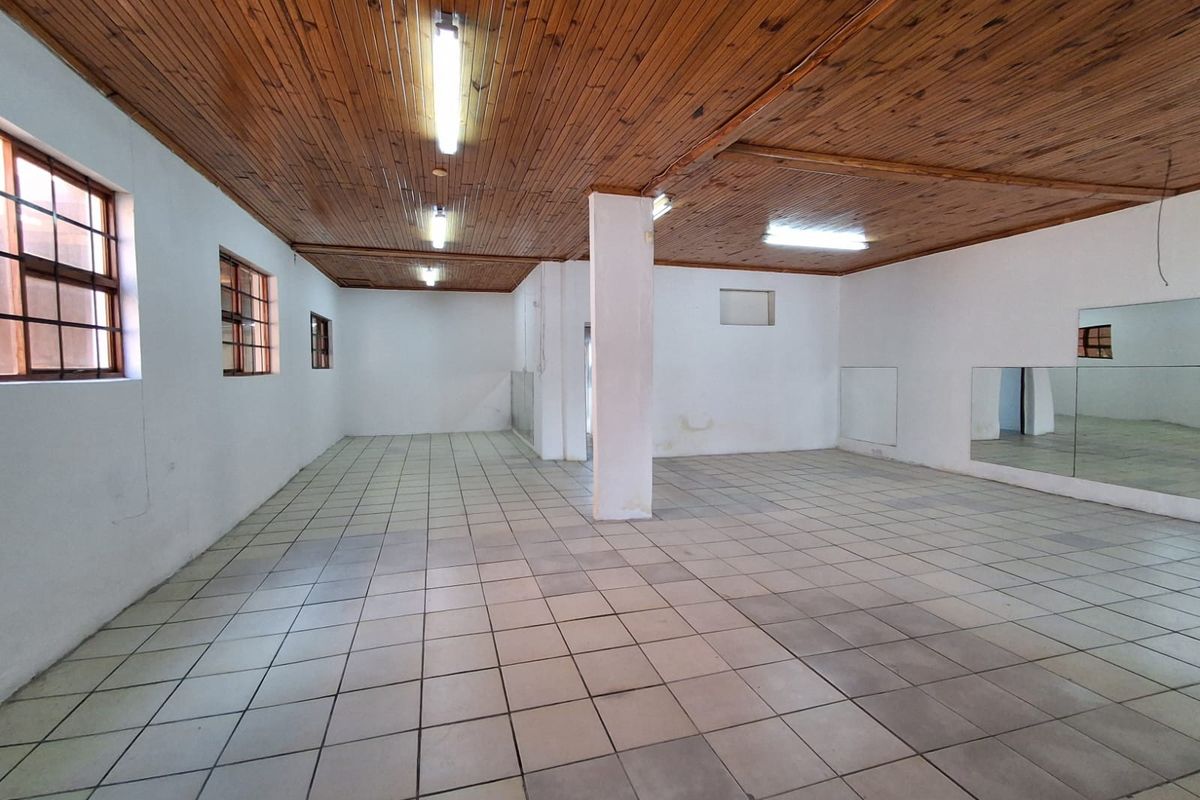 Spacious open-plan industrial area featuring a timber ceiling, ceramic tiled flooring, structural support column, and wall-mounted mirrors, suitable for various commercial or studio uses.