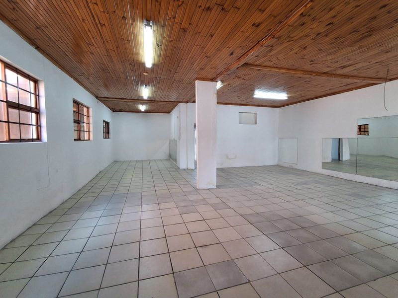 Spacious open-plan industrial area featuring a timber ceiling, ceramic tiled flooring, structural support column, and wall-mounted mirrors, suitable for various commercial or studio uses.