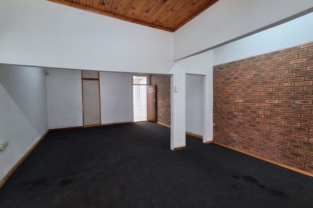 An open-plan office space featuring exposed brick walls, a timber ceiling, and carpeted flooring, providing a versatile industrial-style workspace.