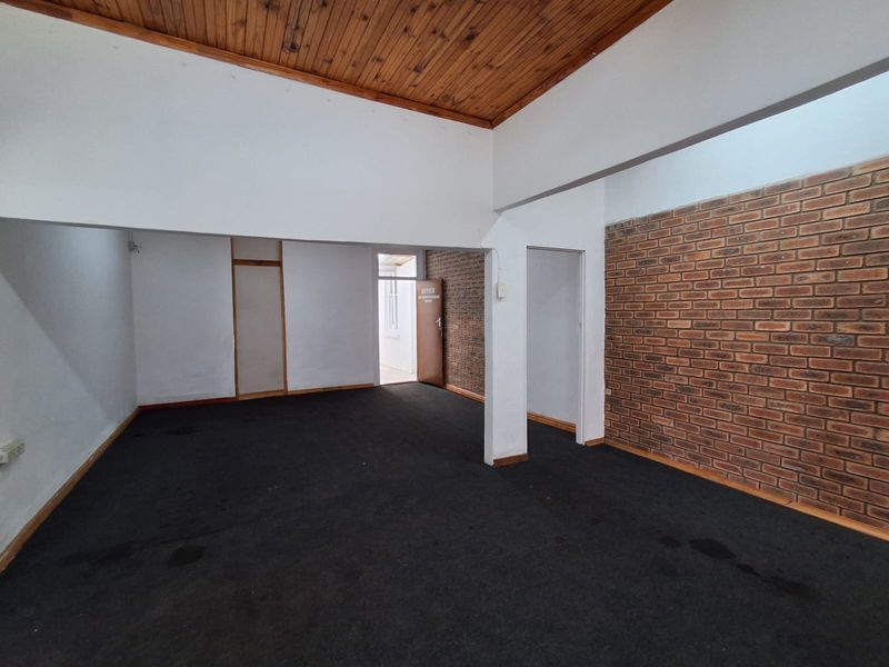 An open-plan office space featuring exposed brick walls, a timber ceiling, and carpeted flooring, providing a versatile industrial-style workspace.