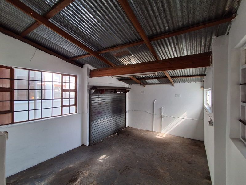 An empty industrial-style garage featuring a corrugated metal roof, exposed timber rafters, a roller shutter door, and steel-framed windows.