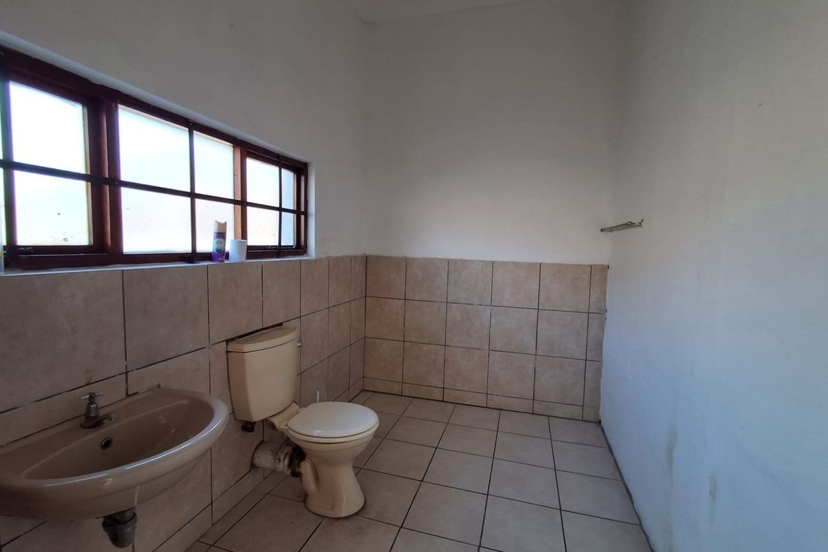 A functional bathroom featuring tiled walls and flooring, a pedestal basin, and a toilet, requiring cosmetic updates to improve its overall condition.