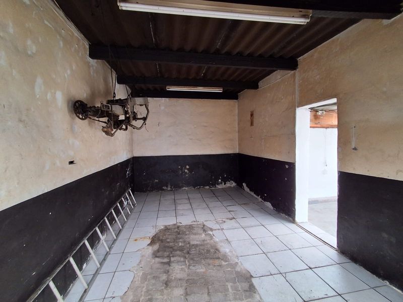 A vacant industrial utility space featuring tiled flooring, exposed beam ceiling, and fluorescent lighting, requiring maintenance and cosmetic updates.