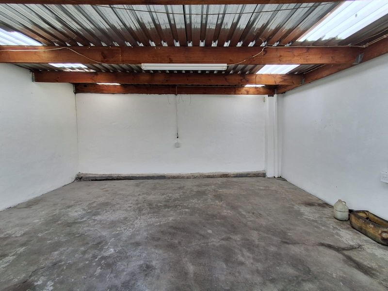 An empty industrial-style garage space featuring exposed timber beams, a corrugated metal roof with translucent panels, and a concrete floor.