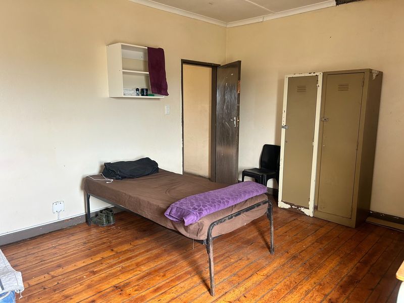 A bedroom featuring original hardwood flooring and a wall-mounted storage shelf, requiring cosmetic updates to improve the overall aesthetic and condition.
