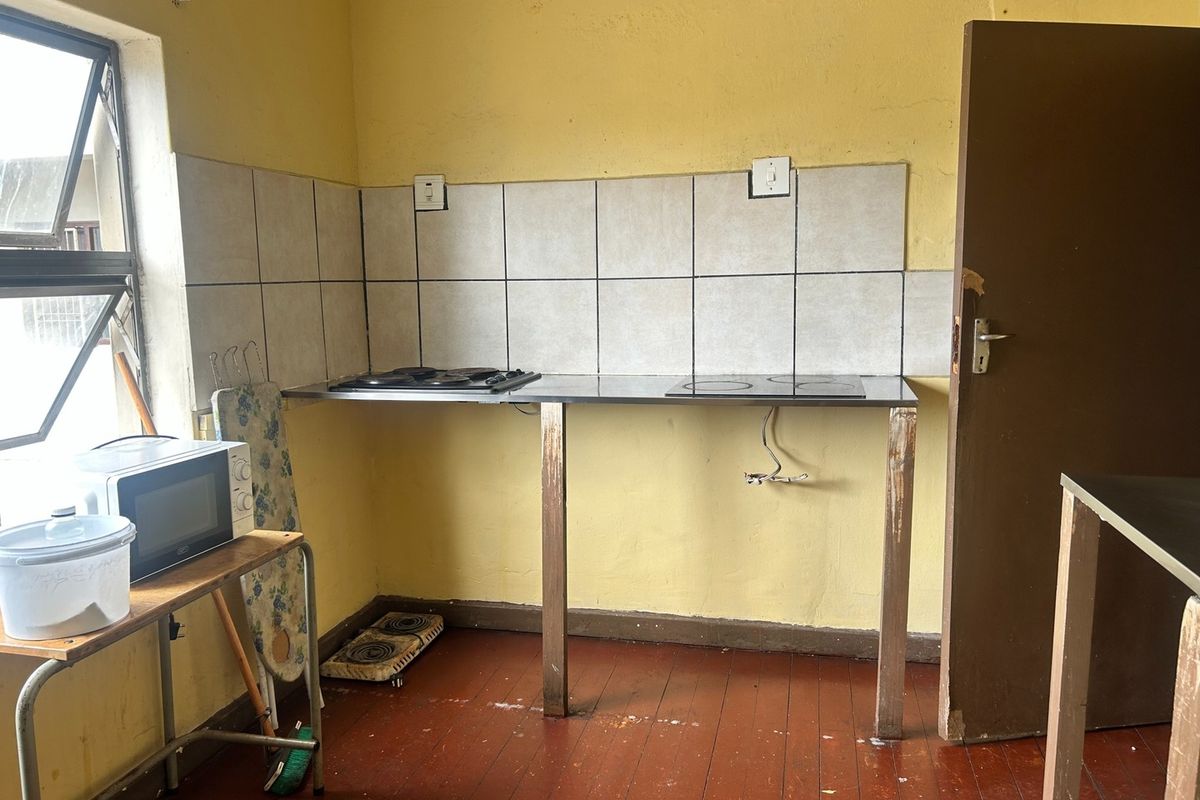 A basic kitchen area featuring a stainless steel countertop with a built-in hob, tiled splashback, and timber flooring in need of renovation.