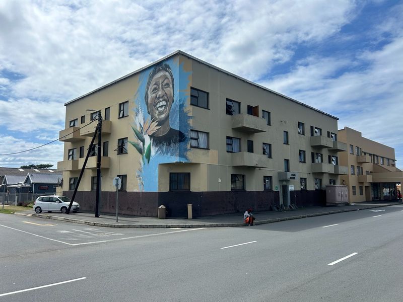 Exterior view of a multi-story apartment building featuring a large mural on the corner facade and multiple balconies.
