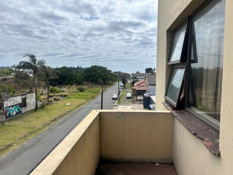 An elevated balcony overlooking a street and surrounding neighborhood, featuring a simple concrete railing and a casement window.