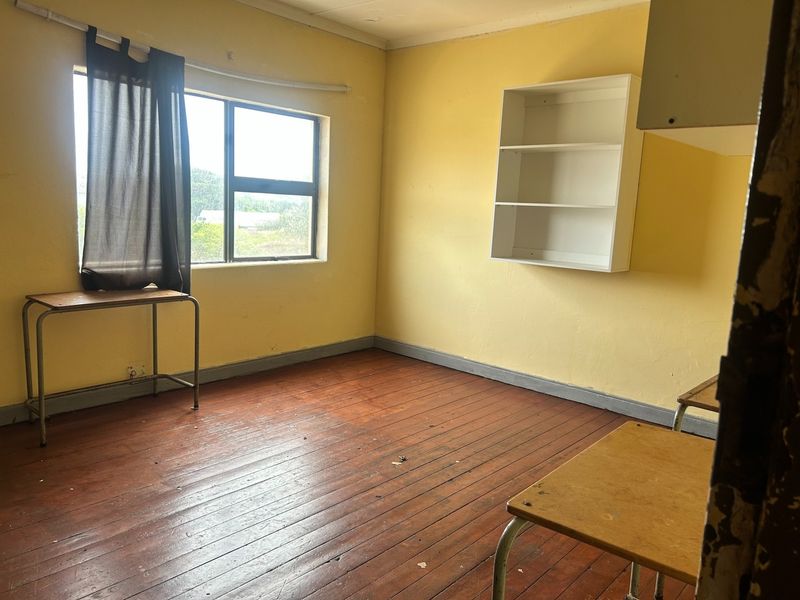 A vacant bedroom featuring original timber flooring, built-in wall shelving, and a window, offering a blank canvas for renovation and modernization.