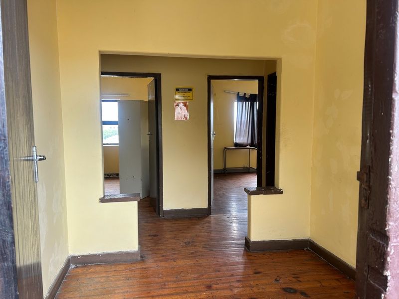 A vacant hallway featuring original hardwood flooring and a pass-through opening, showing signs of wear and requiring cosmetic updates to the wall finishes.
