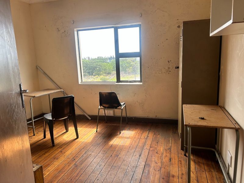A bedroom featuring original timber flooring and an aluminium window, currently requiring significant cosmetic renovation including wall repairs and painting.