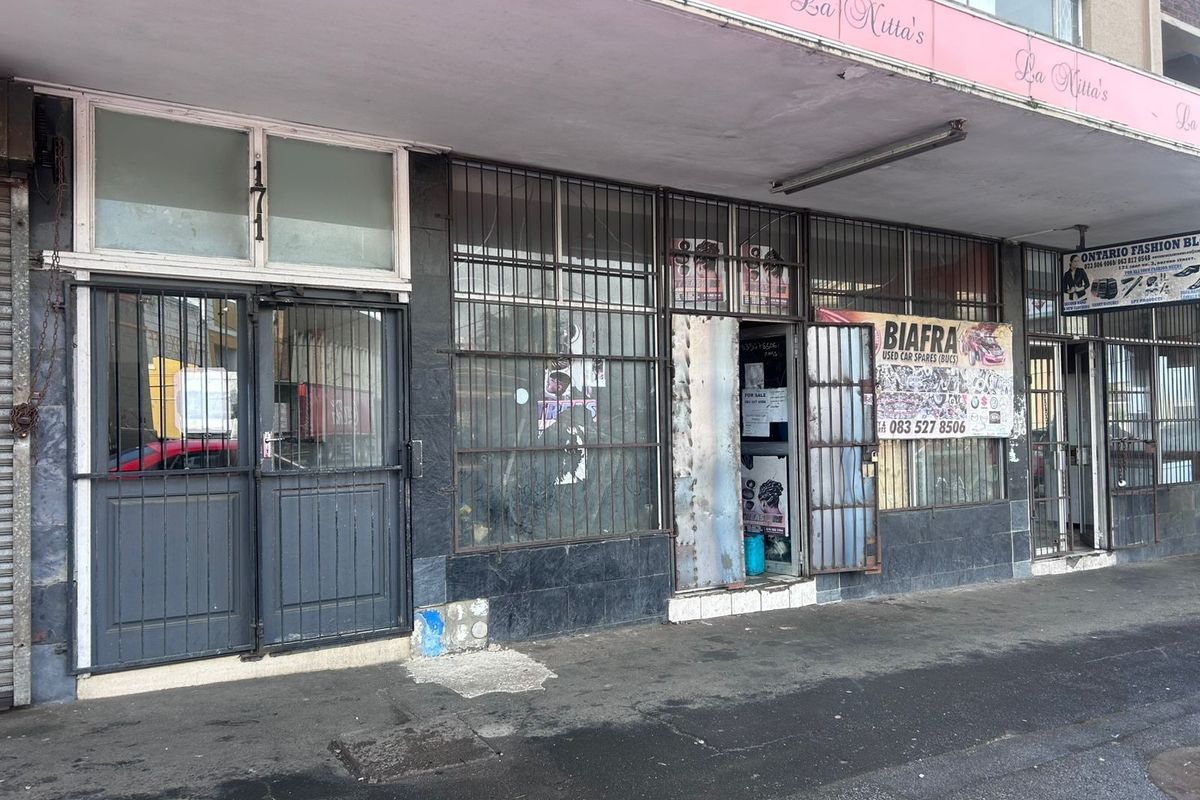 Commercial storefront featuring a tiled facade, security gates, and metal window grilles, located along a covered pedestrian walkway.